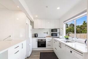 A modern kitchen with white cabinetry, a built-in oven, a microwave, and a sink with a window view.