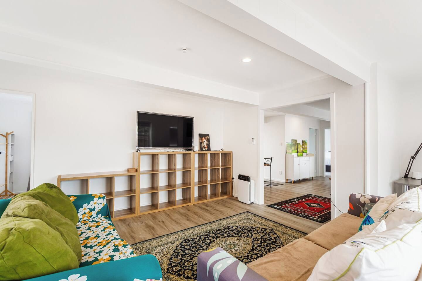 A modern living room with a flat-screen TV, wooden shelving, a sofa, and a patterned rug.