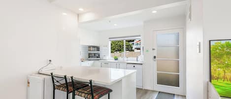 A modern kitchen with white cabinetry, a central island with bar stools, and a view of the outside.