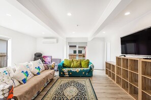A modern living room with a sofa, a green sofa, a TV, and a wooden cabinet.