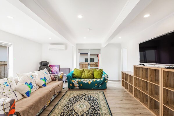 A modern living room with a sofa, a green sofa, a TV, and a wooden cabinet. - Spacious Renovated 3BR in Ellerslie I Zodiak Stays (Auckland)