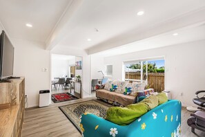 A modern living room with a sofa, a dining area, and a kitchen in the background.