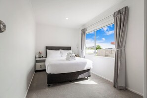 A hotel room with a bed, a nightstand, a window with curtains, and a view of the outside.