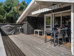 Une terrasse avec une table et des chaises, un barbecue couvert et une porte vitrée donnant sur un espace extérieur.