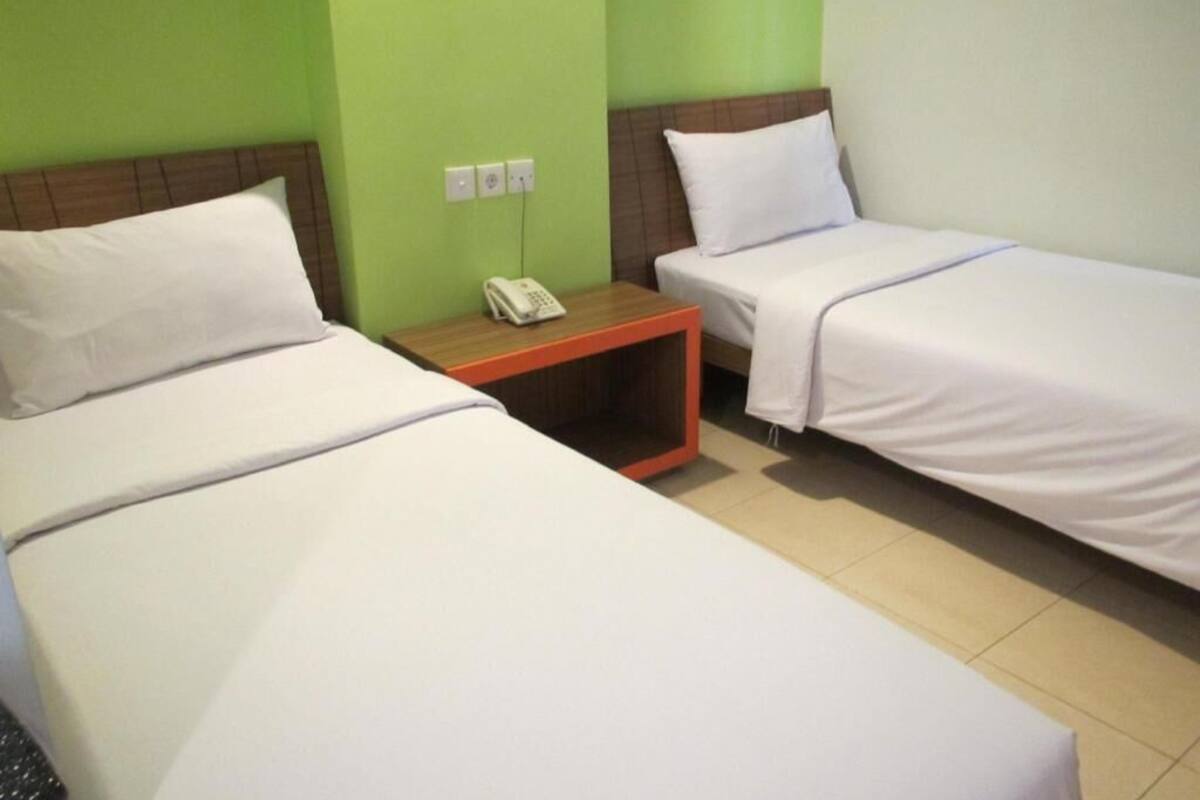 A hotel room with two beds, a nightstand with a phone, and green walls.