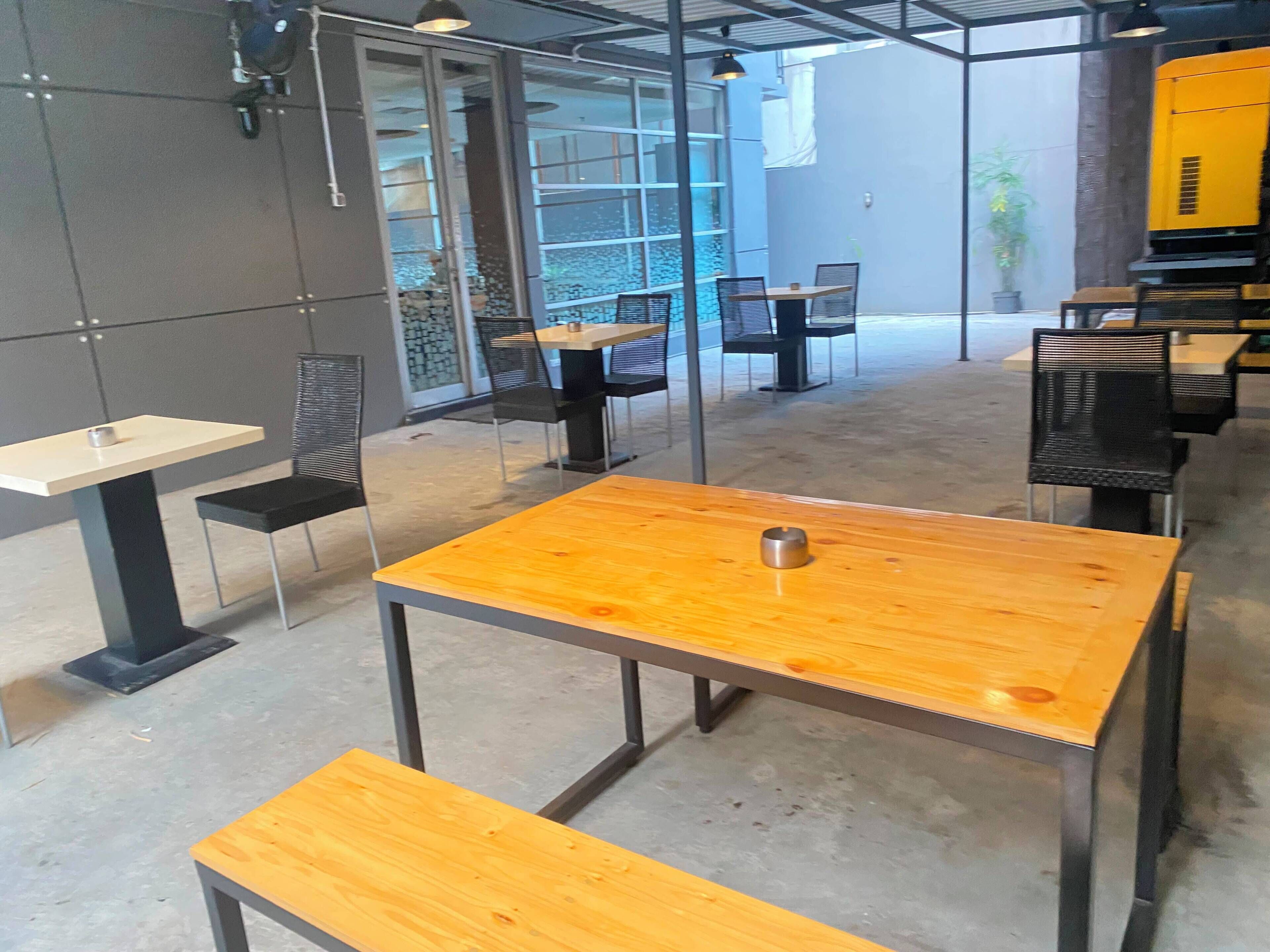 Un área de estar interior moderna con mesas y sillas, separadores de vidrio y un espacio exterior visible.