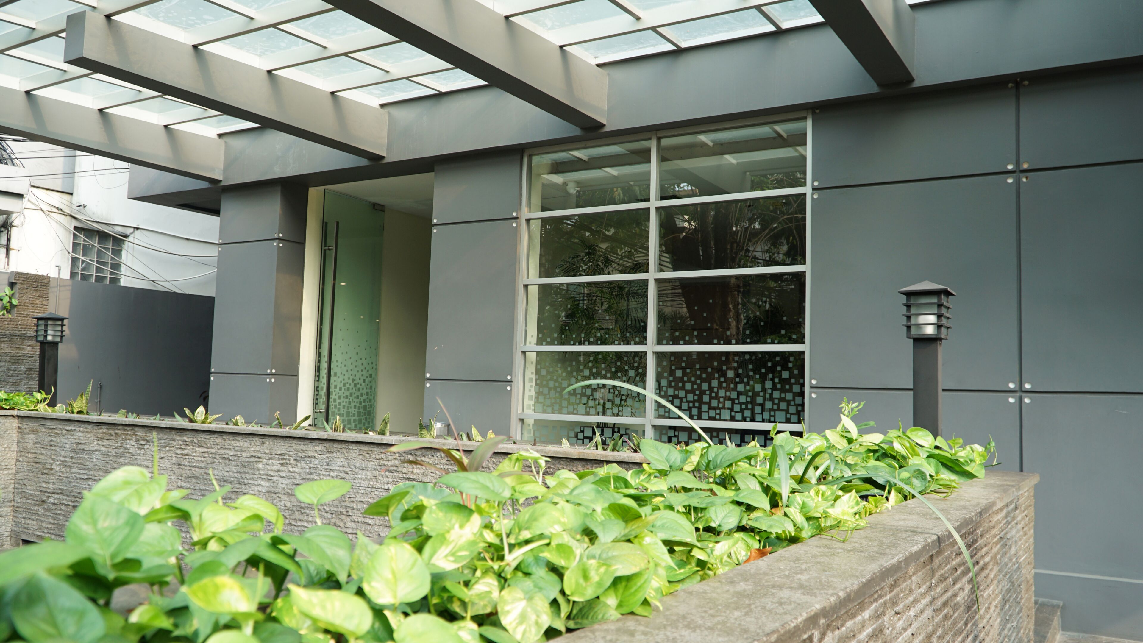 A modern building with a large glass window, a stone wall with greenery, and a metal structure above.