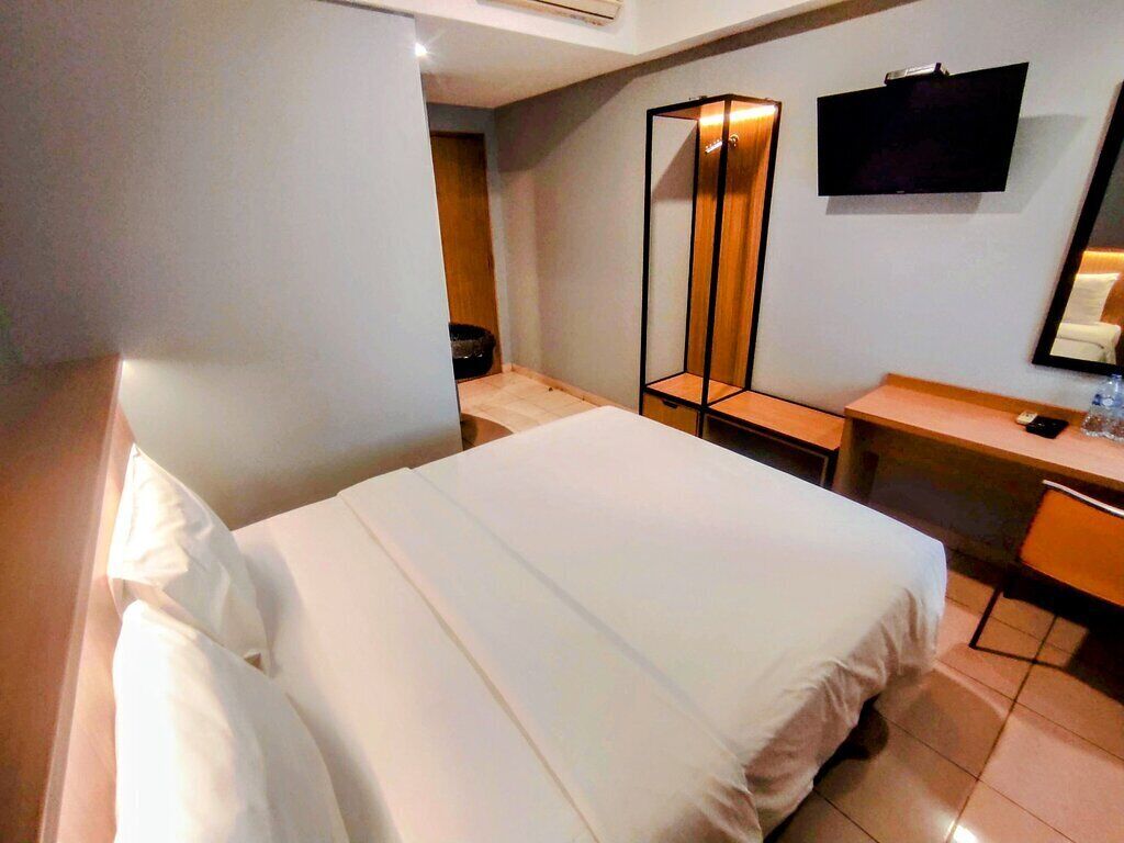 A hotel room with a bed, a desk, a chair, a TV, and a mirror.