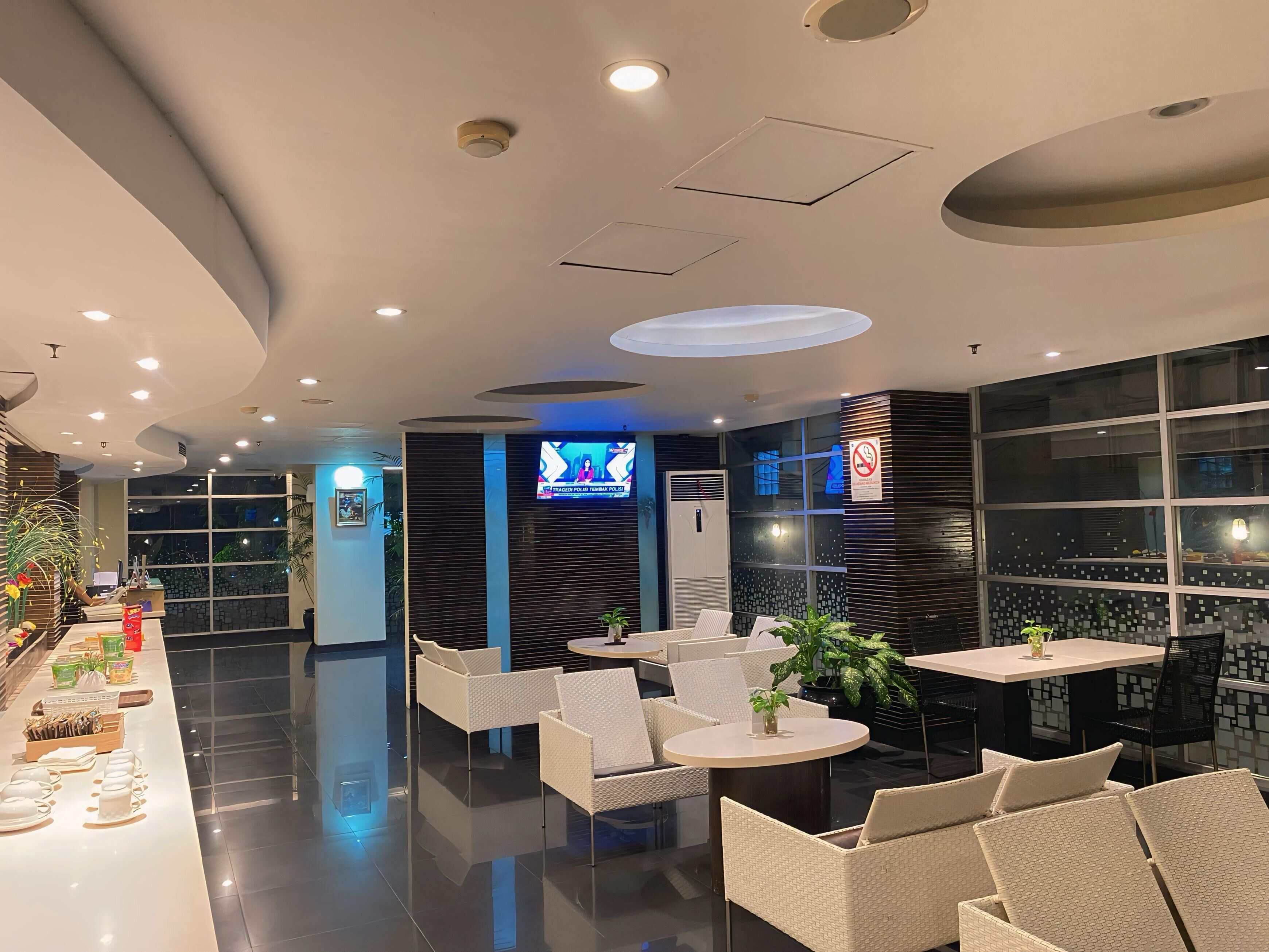 A modern hotel lobby with a reception desk, seating area, and a TV screen displaying a news program.