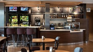 Eine moderne Bar mit verschiedenen Sitzgelegenheiten, einer Kaffeemaschine sowie einer Auswahl an Getränken und Snacks.