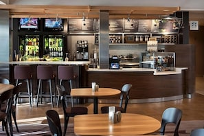 Eine moderne Bar mit verschiedenen Sitzgelegenheiten, einer Kaffeemaschine sowie einer Auswahl an Getränken und Snacks.