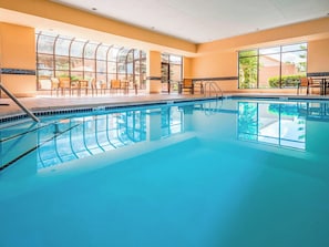 Ein überdachter Schwimmbereich mit Glaswänden, gefliestem Boden und einer Sitzgelegenheit mit Stühlen und Tischen.