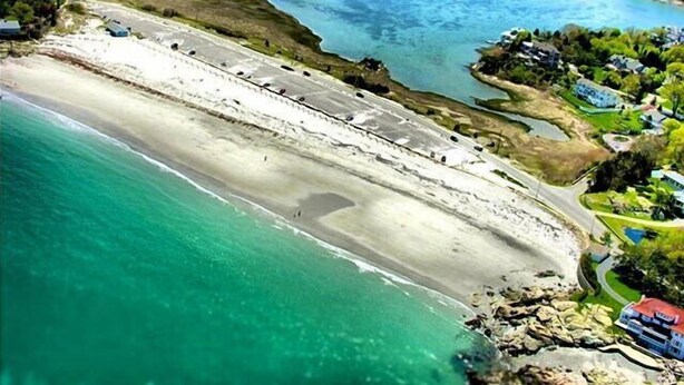 Ein Luftbild einer Küstenregion mit Sandstrand, klarem blauen Wasser und verstreuten Gebäuden.