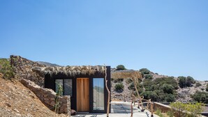 Un edificio moderno con entrada de techo de paja, paredes de piedra y un gran ventanal.