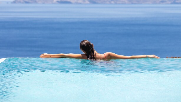 Una persona relajándose en una piscina azul cristalina, con vistas a montañas al fondo.