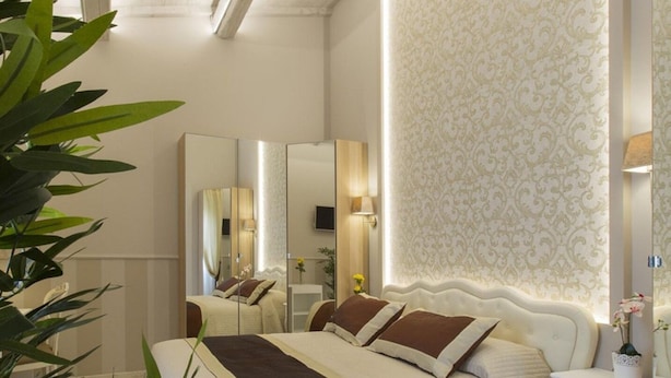 A bedroom with a large bed, a nightstand, a mirror, and a wall with a decorative pattern. - Beautiful Central Apartment (Firenze)