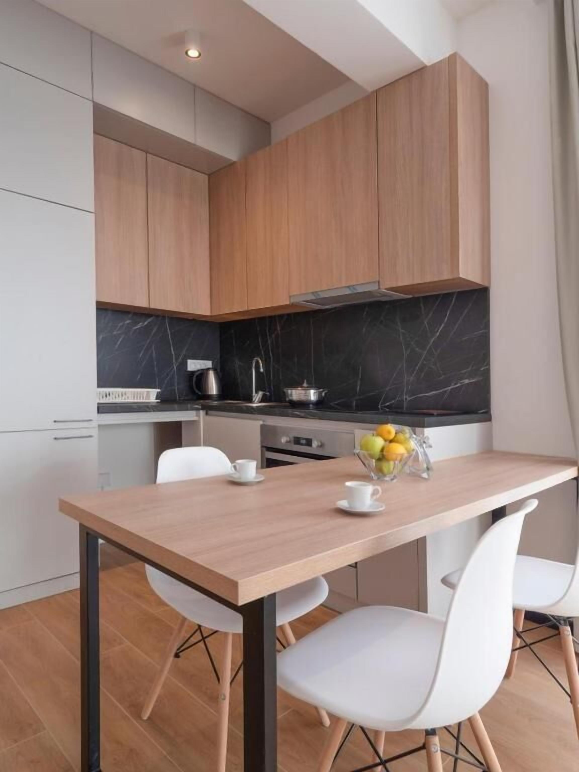 Une cuisine moderne avec des meubles en bois, un plan de travail en marbre et un coin repas comprenant une table en bois et des chaises blanches.