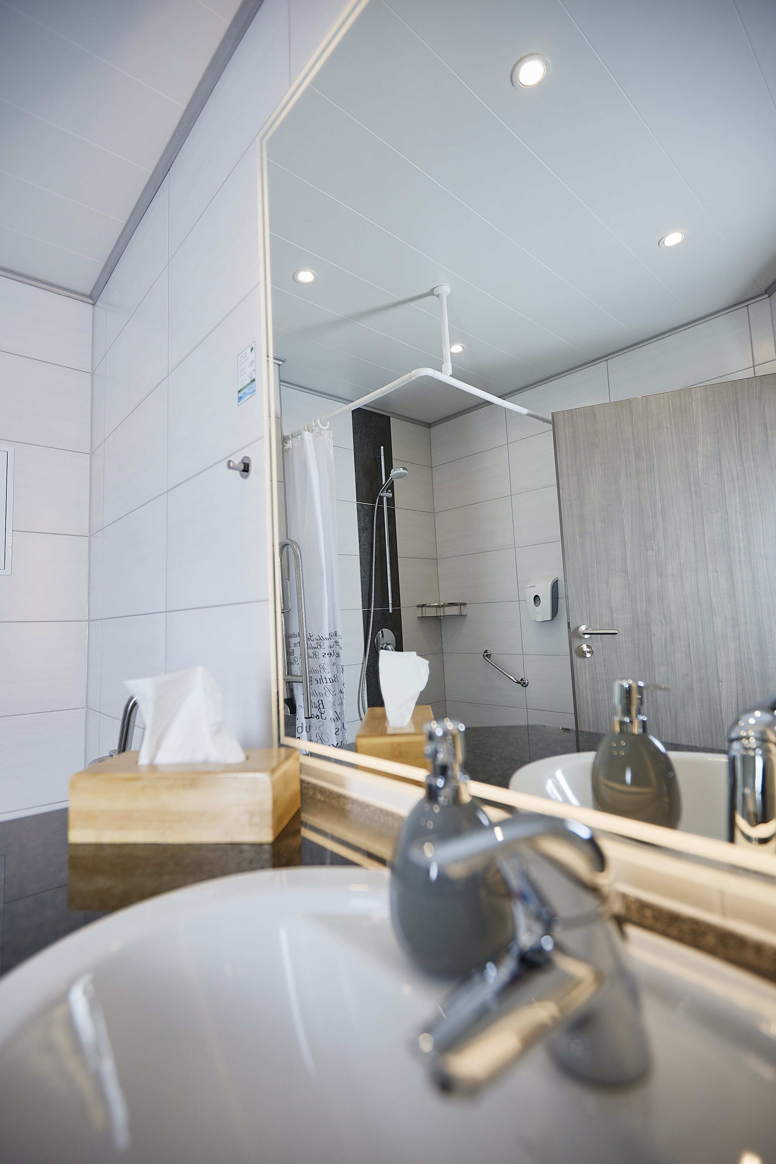 Une salle de bain moderne dotée d’un grand miroir, de deux lavabos, d’une douche et d’un distributeur de serviettes.