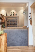 Un área de recepción con mostrador de madera, botellas de vino y una planta colgante.