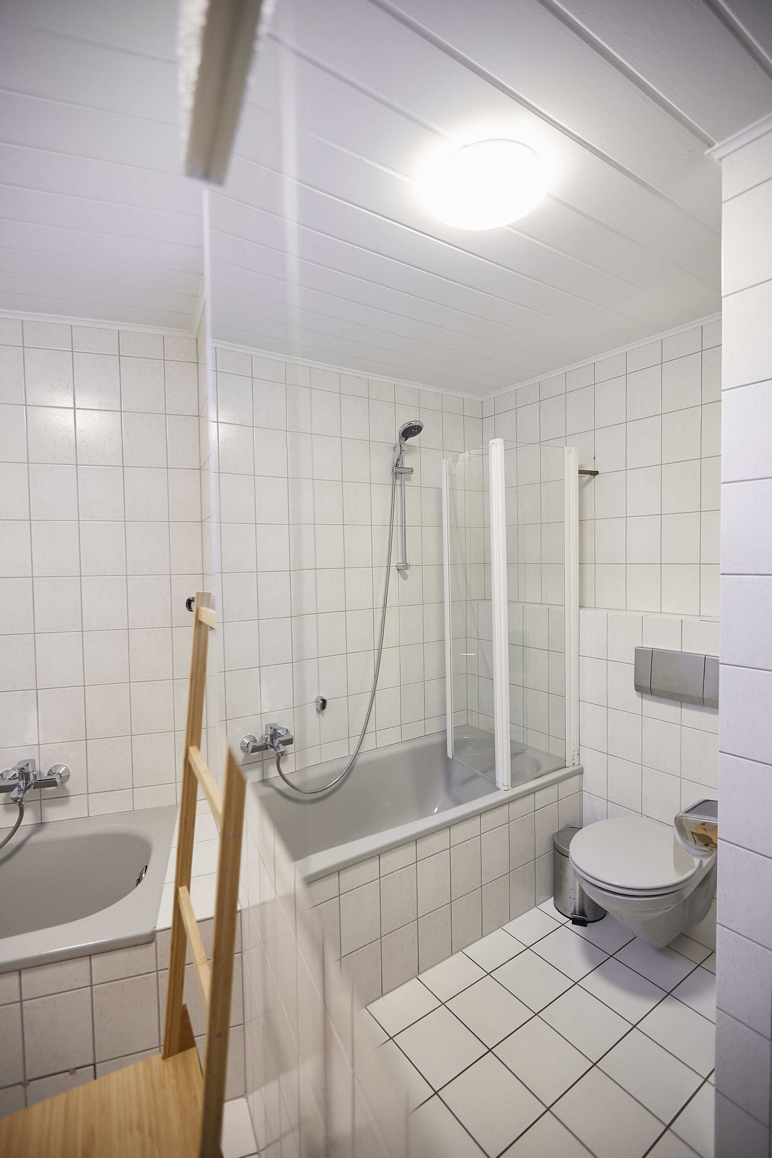 A bathroom with white tiled walls, a bathtub, a shower, and a toilet.