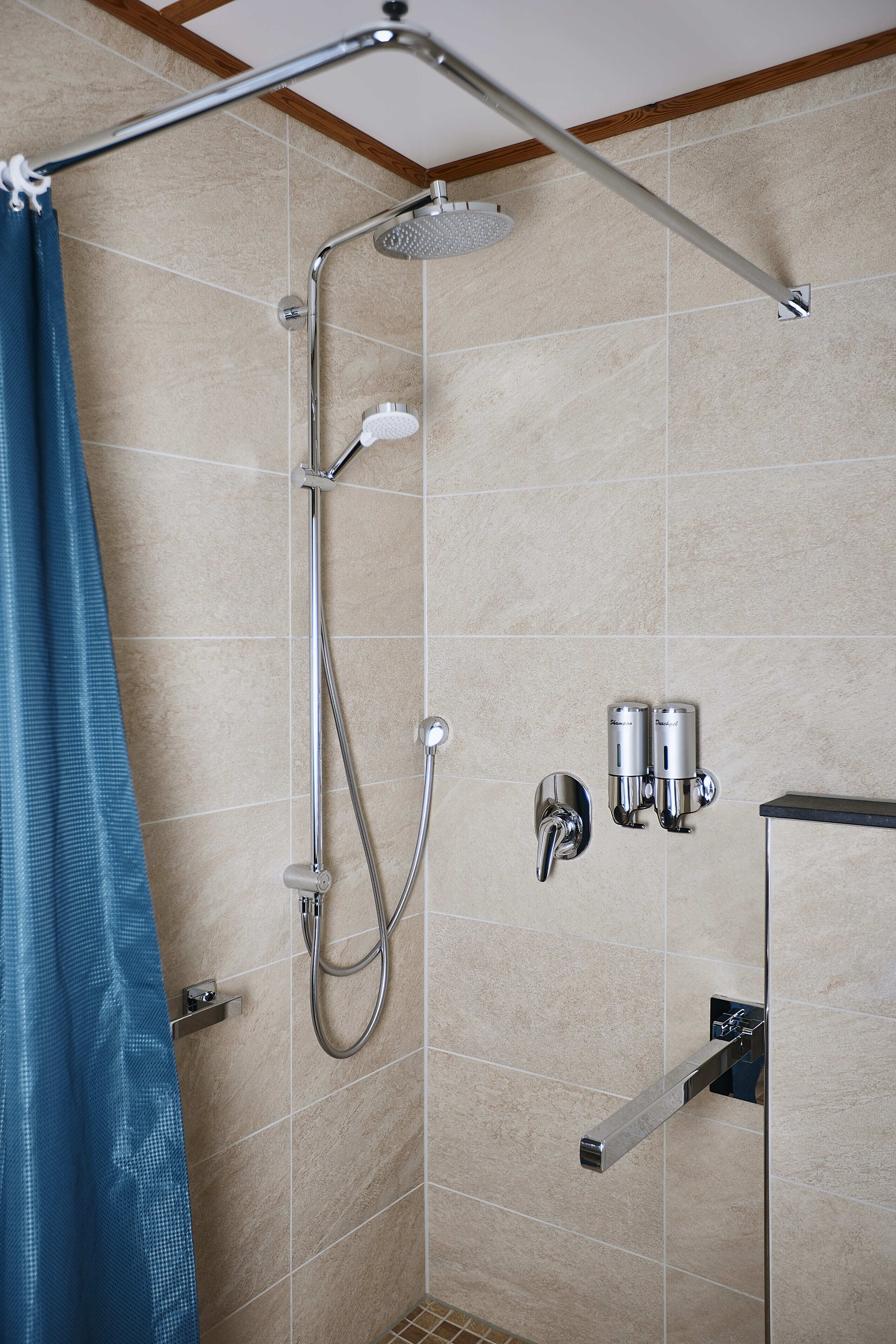 A shower area with a handheld showerhead, a wall-mounted faucet, and two wall-mounted water dispensers.