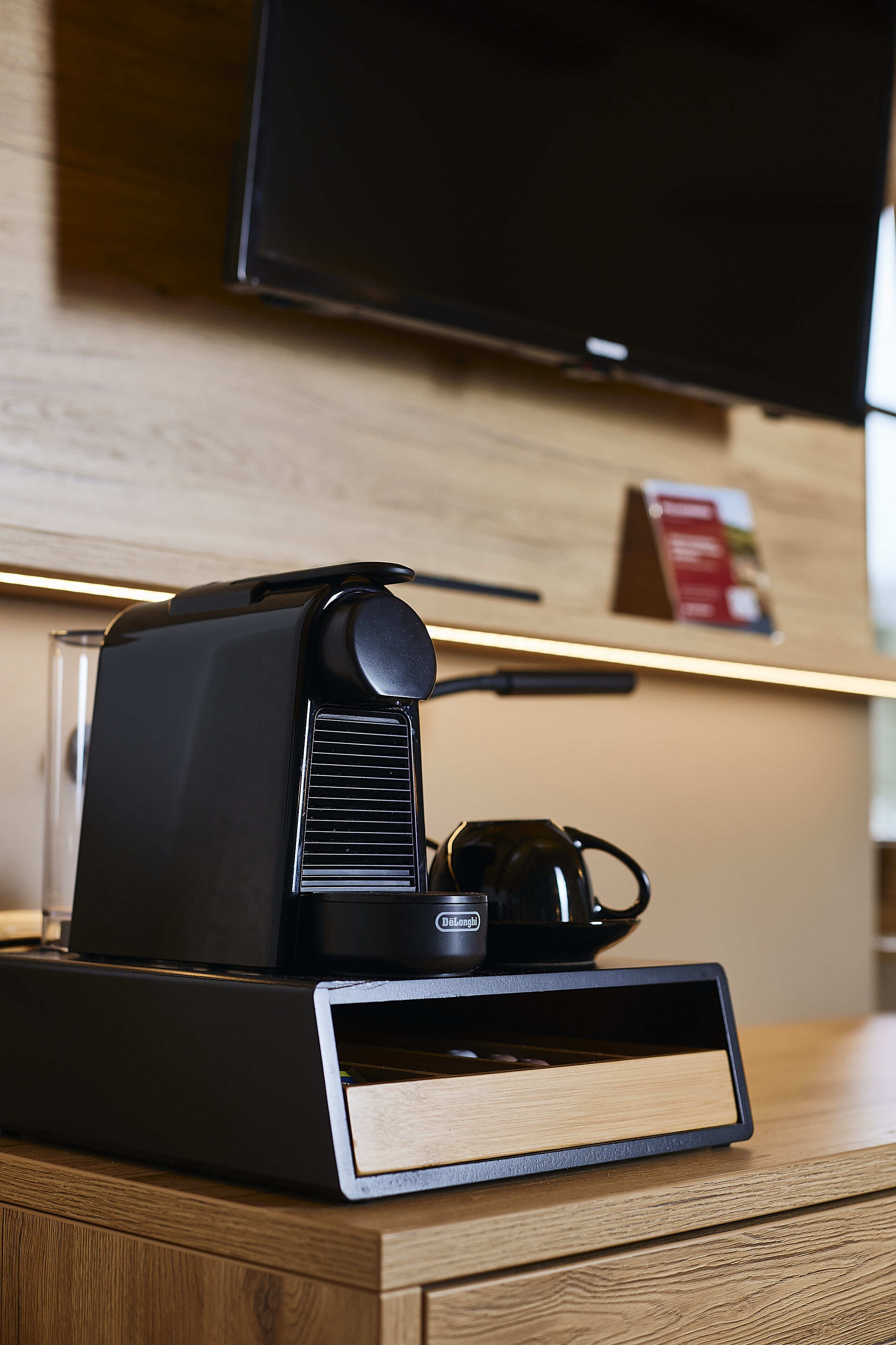 Une machine à café est posée sur un comptoir en bois, et un téléviseur à écran plat est fixé au mur juste au-dessus.