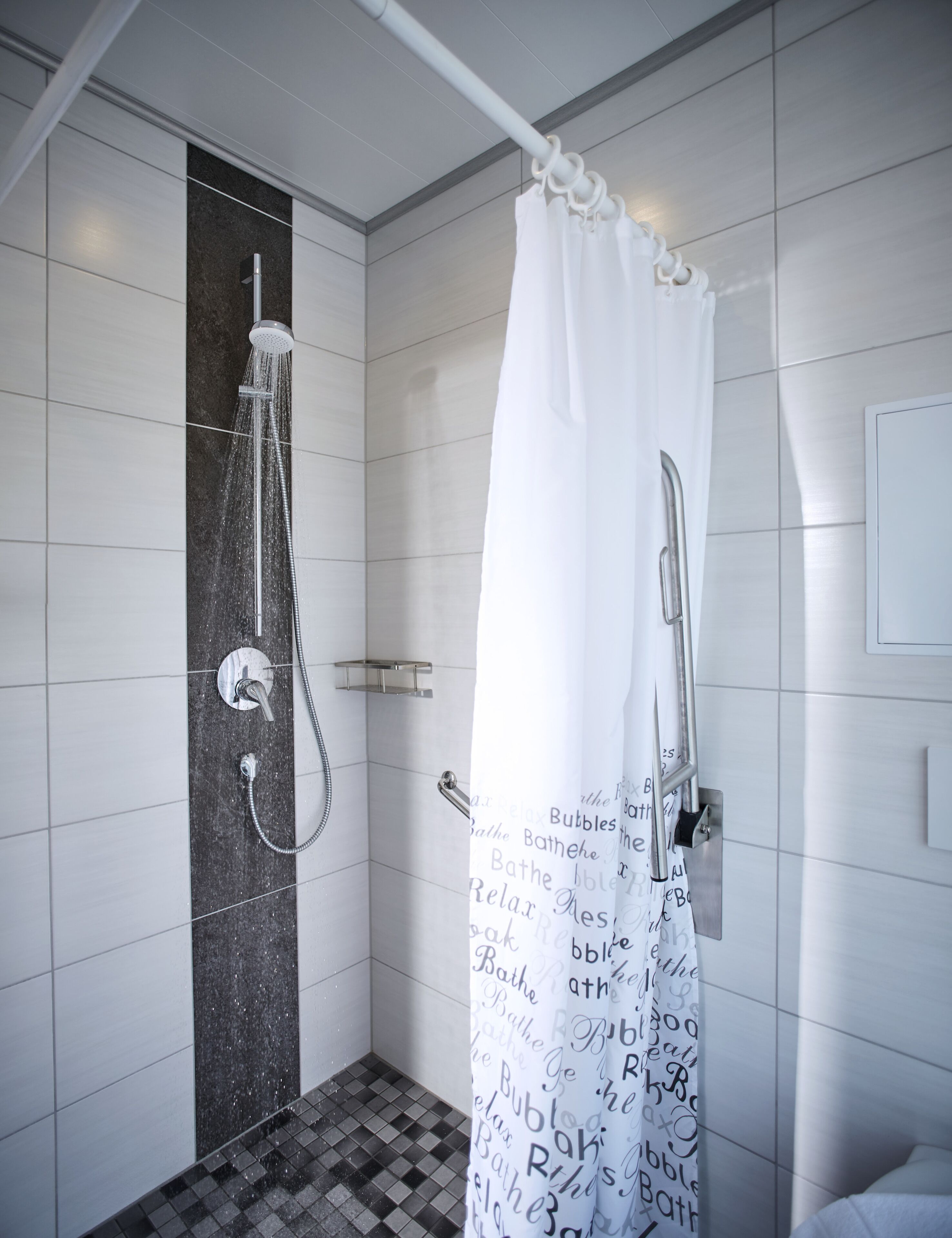 Ein modernes Badezimmer mit Dusche, einem weißen Vorhang mit Schriftzug und Fliesenwänden.
