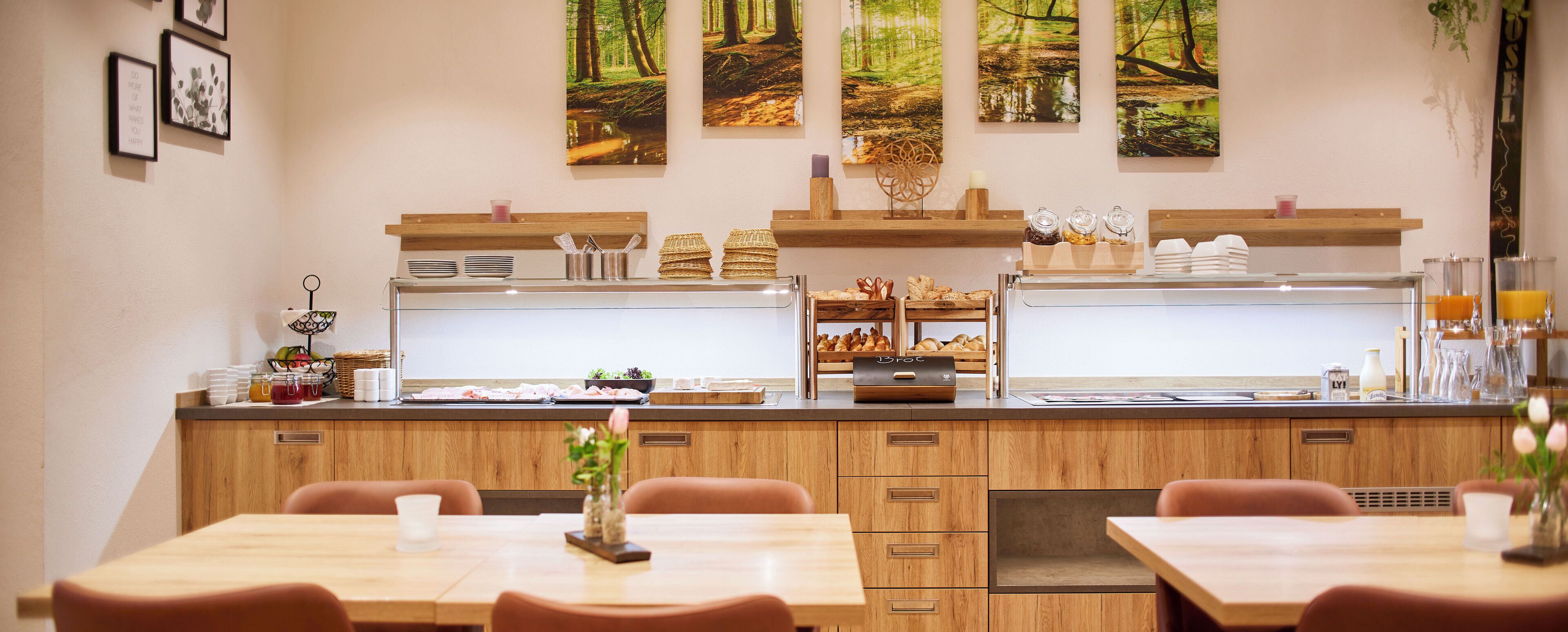 A restaurant with wooden cabinets, a counter with food items, and a view of a forest through the window.