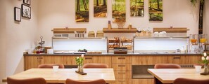 A restaurant with wooden cabinets, a counter with food items, and a view of a forest through the window. - Weinhaus Lenz (Briedern)
