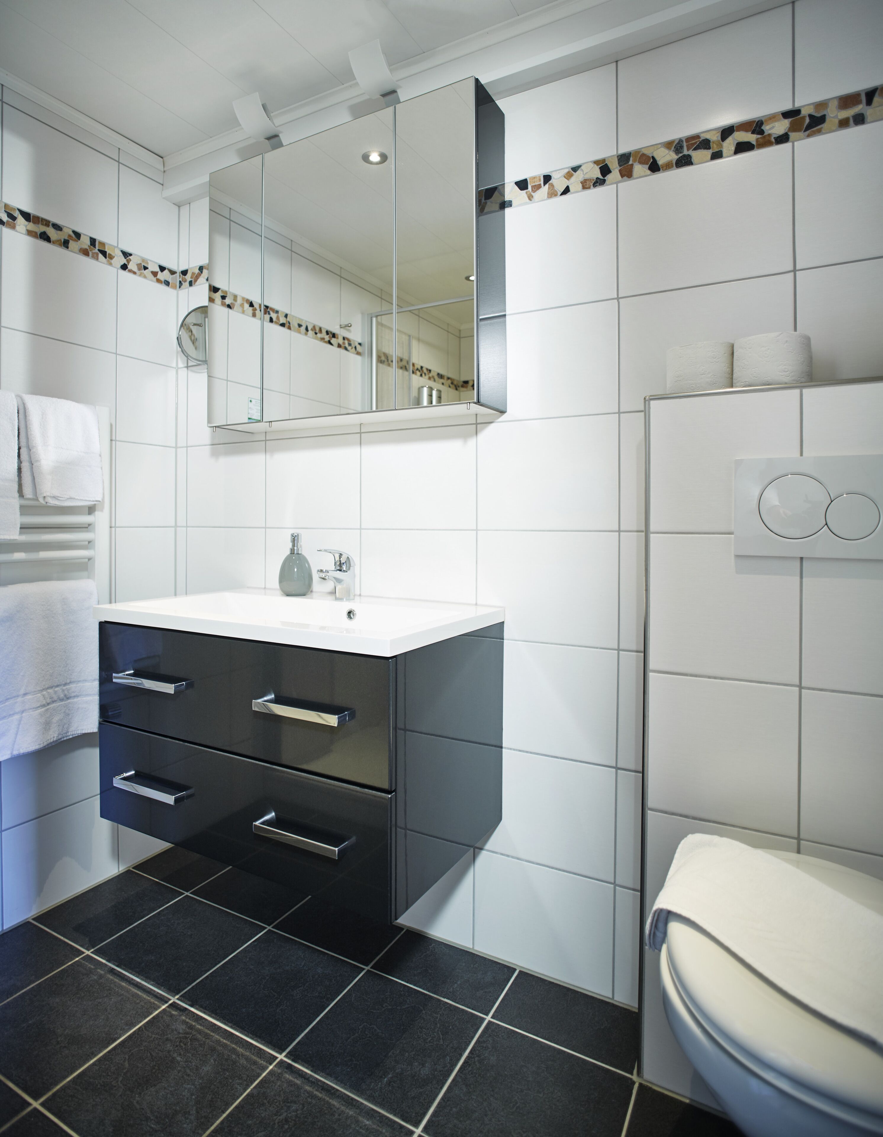 Een moderne badkamer met een wit wastafelmeubel, zwarte lades, een spiegel en een toilet.