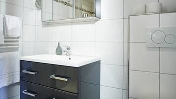 Een moderne badkamer met een wit wastafelmeubel, zwarte lades, een spiegel en een toilet.