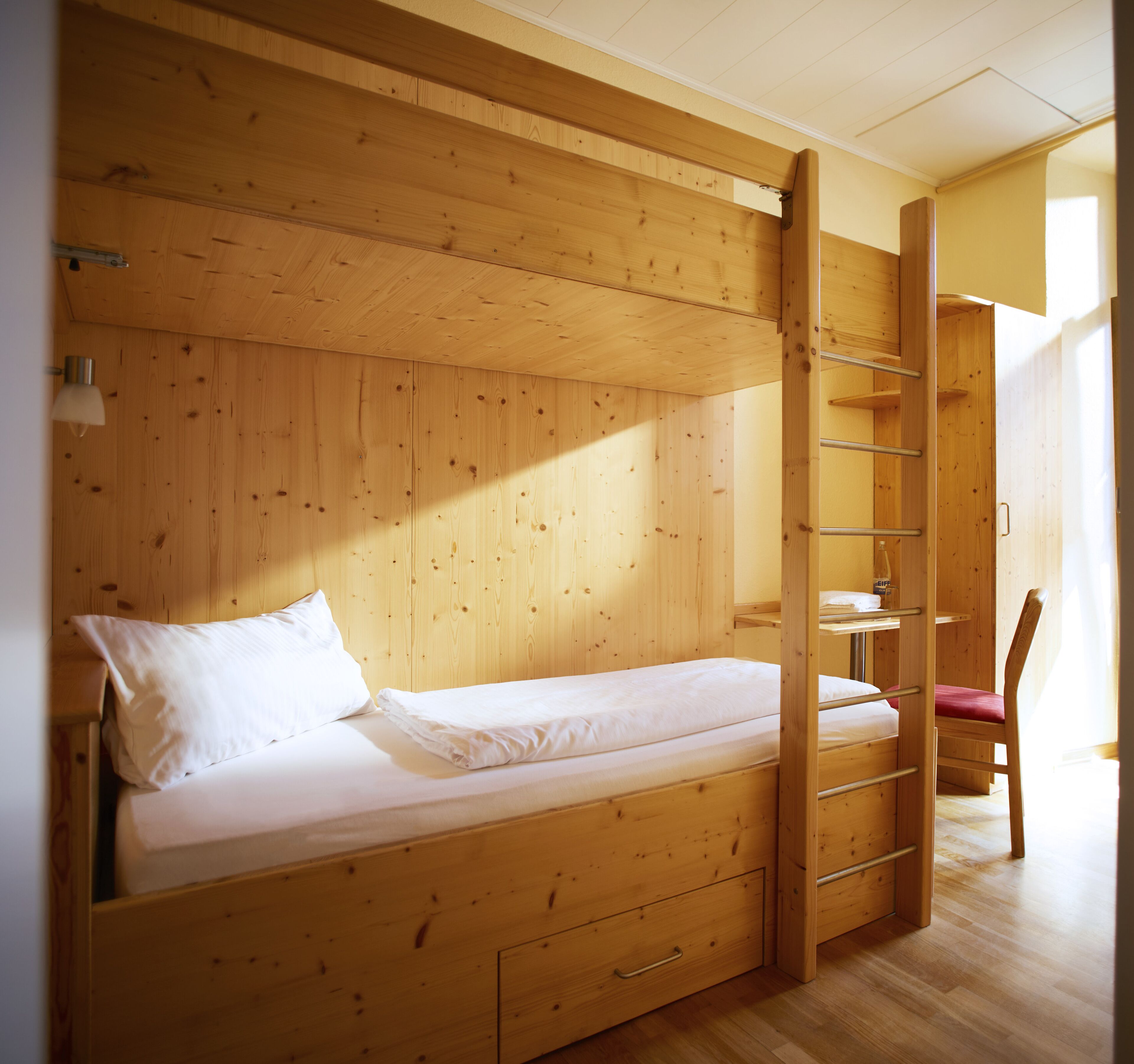 A bunk bed with a ladder, a desk, and a chair in a wooden room.