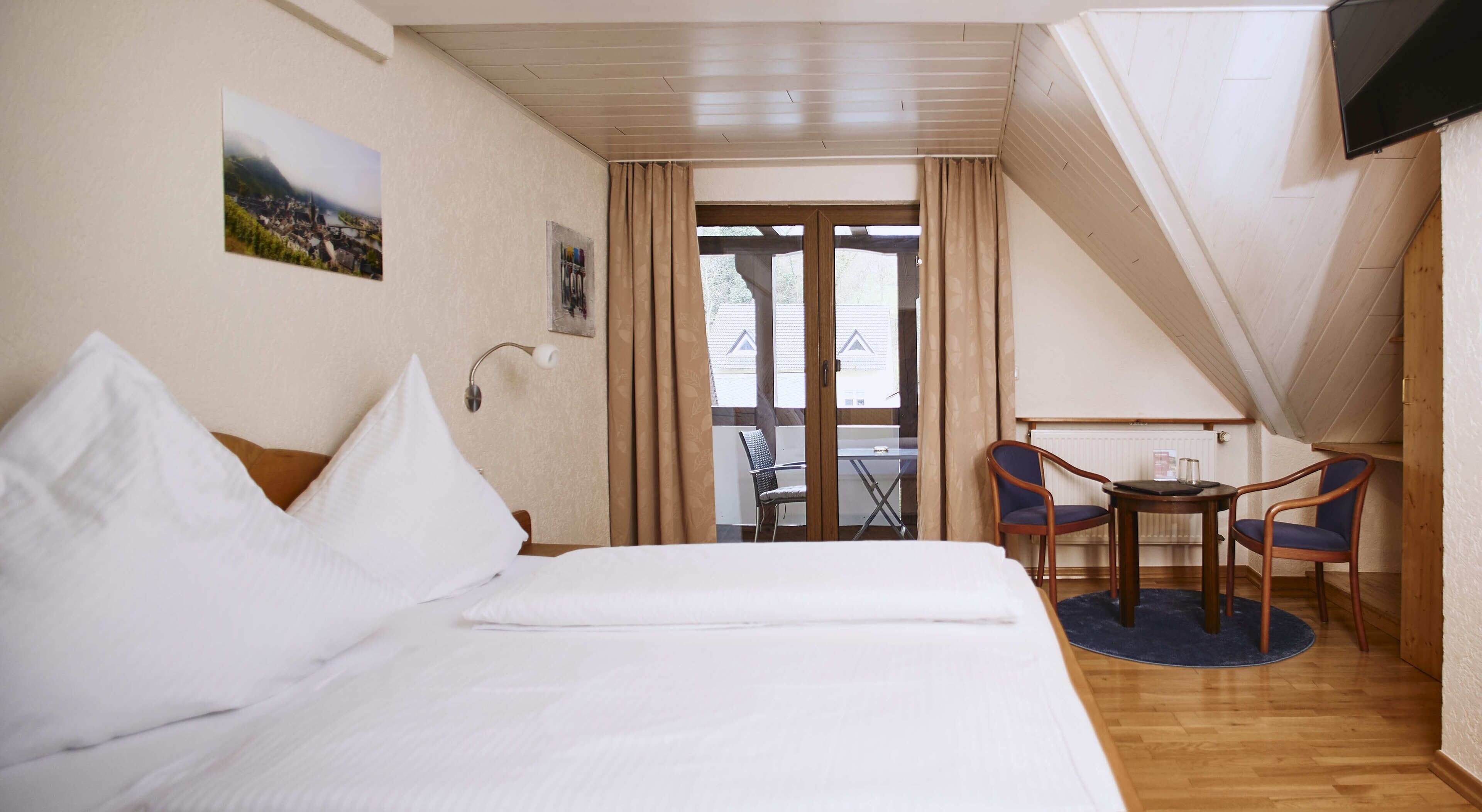A bedroom with a bed, a small table, two chairs, and a TV.
