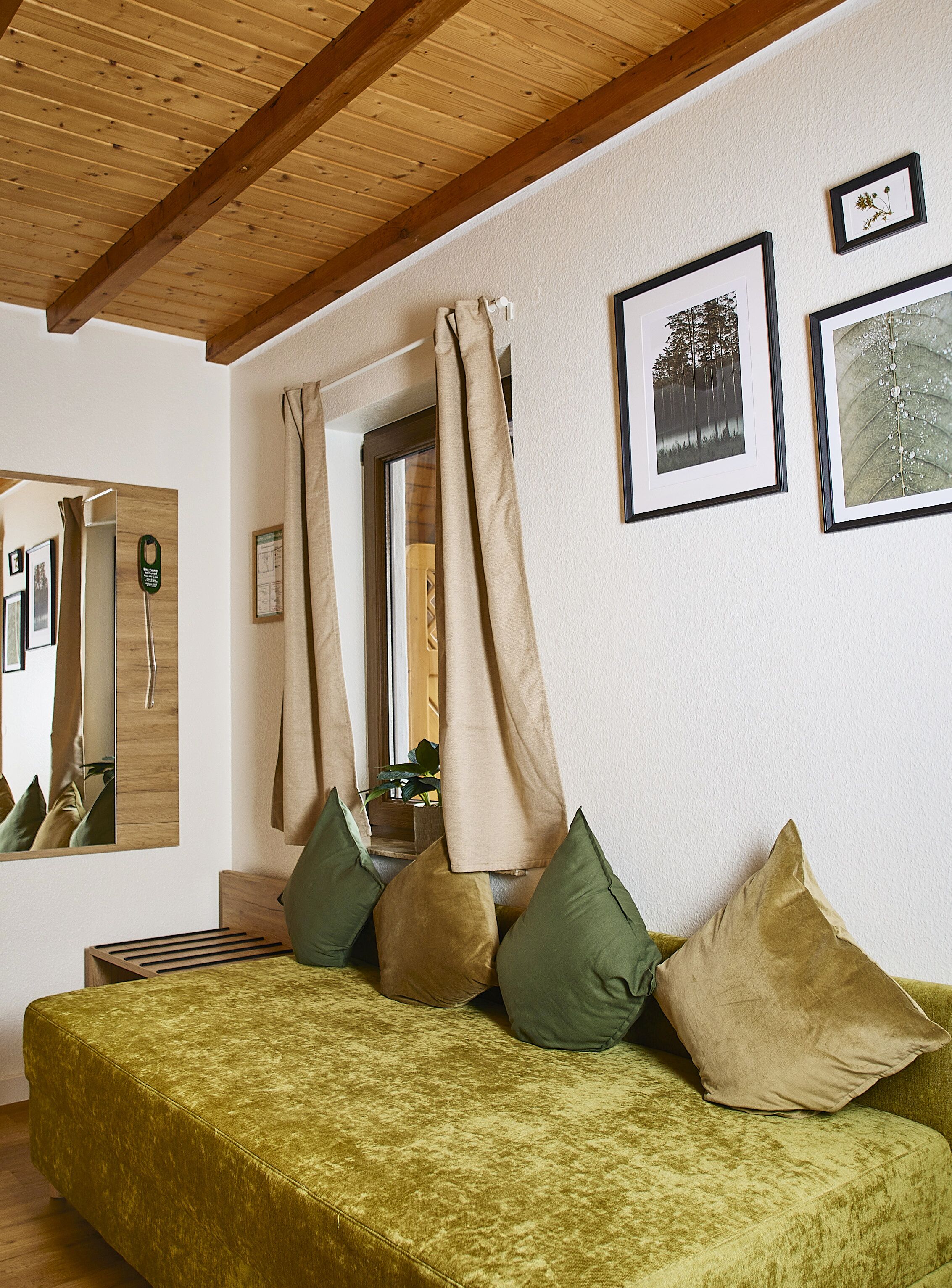 A room with a green sofa, beige curtains, and framed pictures on the wall.