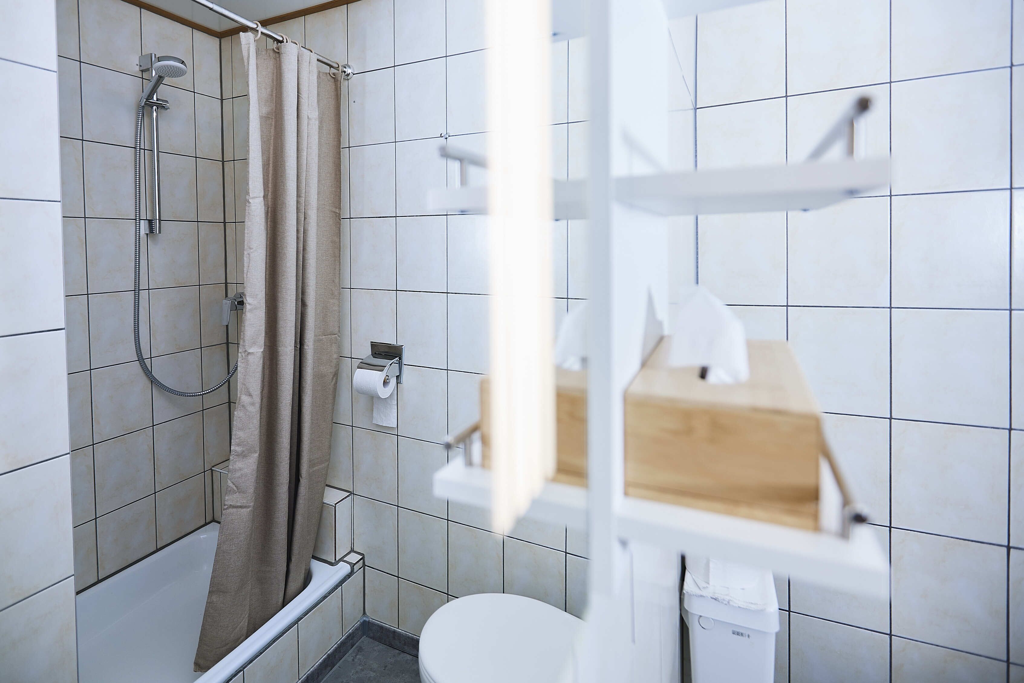A bathroom with a shower, toilet, and a shelf with a box.