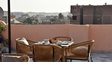 Terraza en la azotea con mobiliario de mimbre, una mesa dispuesta para comer y vistas de la ciudad.