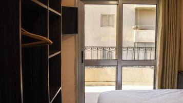 A room with a bed, a wardrobe, a television mounted on the wall, and a balcony with a railing.