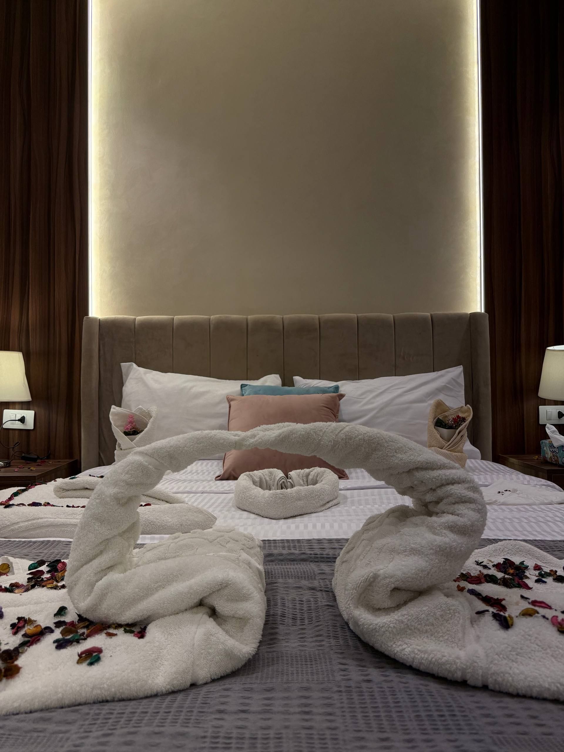 Een hotelkamer met een bed, kussens, een nachtkastje en een handdoeksculptuur.