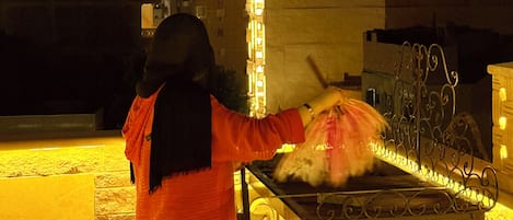 Una persona indossa un lungo abito arancione e sta in piedi di fronte a una griglia metallica con cibo sopra.
