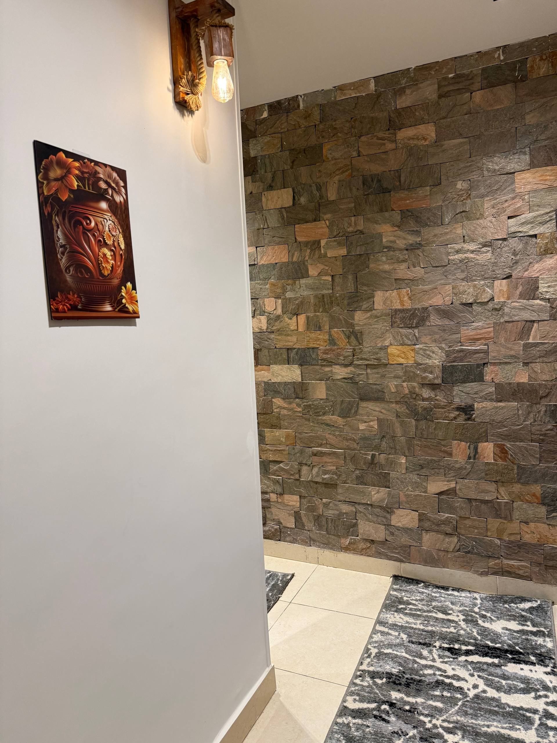 A hallway with a stone wall, a framed artwork, and a patterned rug.