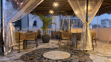 Un área de estar techada al aire libre con muebles de mimbre, una planta en maceta central y un suelo de mosaico.
