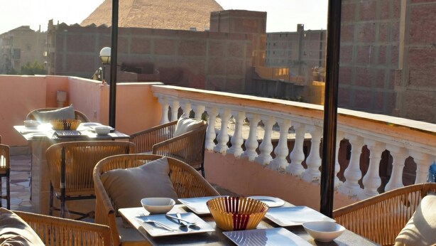A rooftop terrace with wicker furniture, a dining table set with plates, bowls, and cutlery, and a decorative bowl.