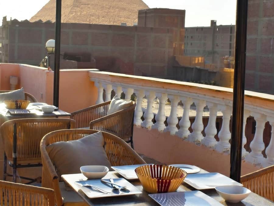 Una terraza en la azotea con mobiliario de mimbre, una mesa de comedor con platos, tazones y cubiertos, y un cuenco decorativo.