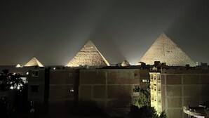 Three illuminated pyramids at night with buildings in the foreground.