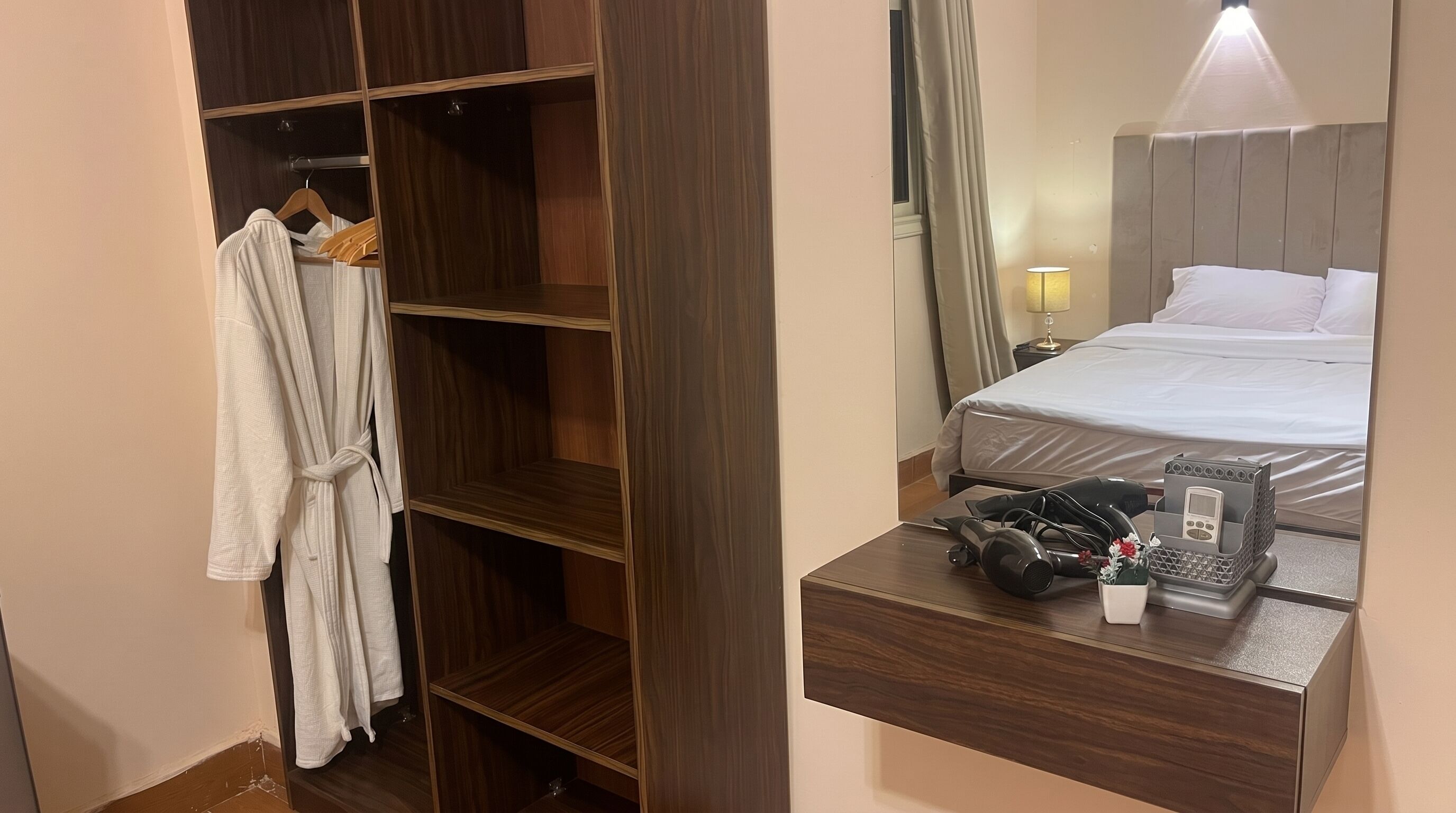 A hotel room with a wooden wardrobe, a bed with white linens, a bedside table with a hairdryer and a phone, and a mirror reflecting the room.