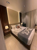 A hotel room with a large bed, bedside lamps, a nightstand, and a view of the city through curtains.