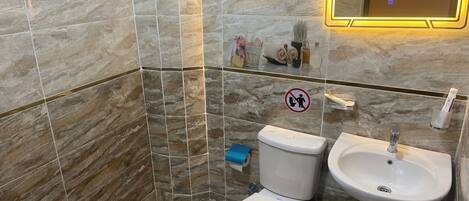 A bathroom with marble walls, a sink, toilet, and a hand dryer.