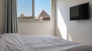 A room with a bed, a window with a view of pyramids, and a mounted TV.