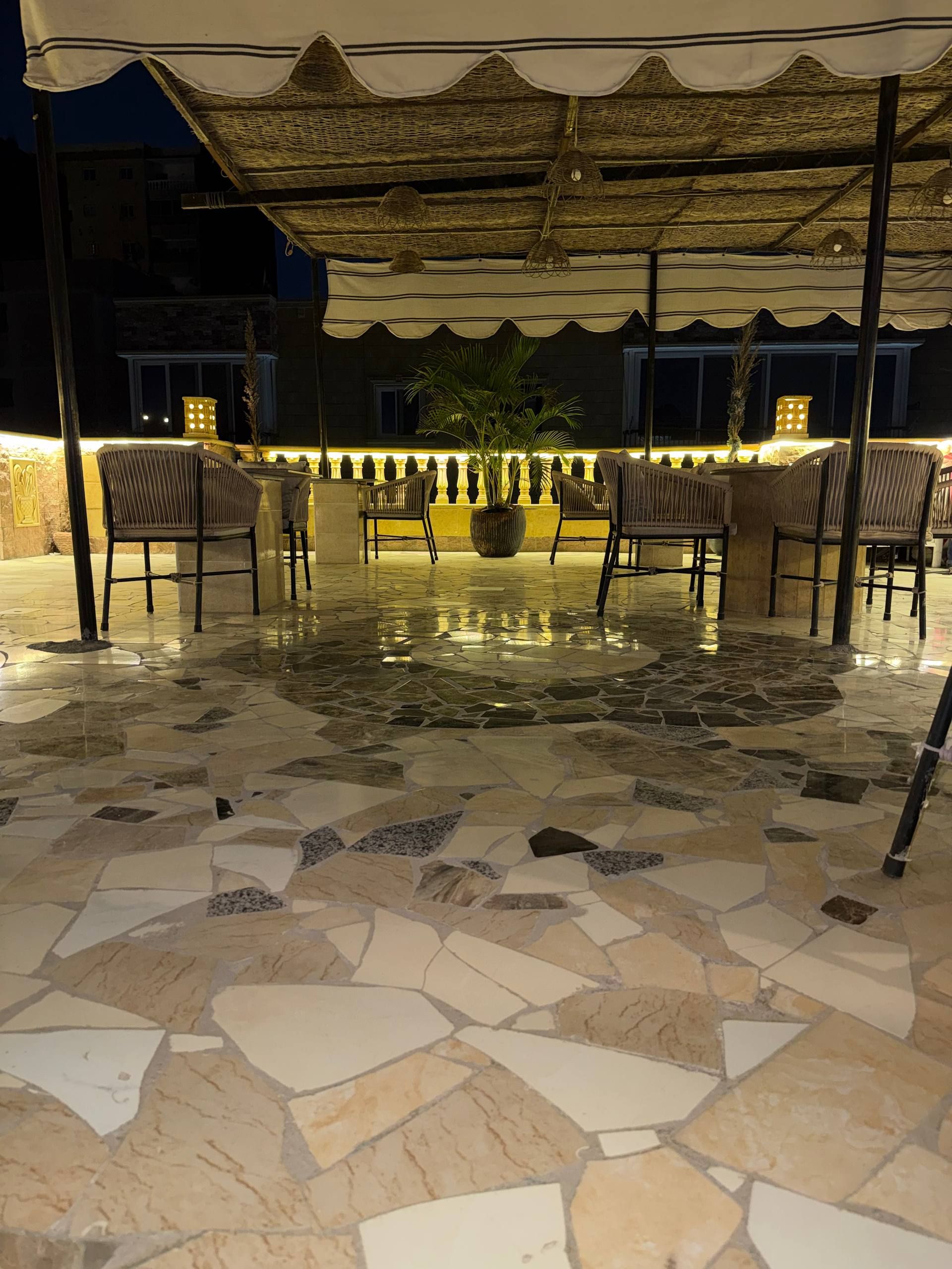 Un espace extérieur aménagé avec des sièges, un sol en pierre et des chaises en osier, situé sous une partie couverte dont le plafond est orné de motifs.
