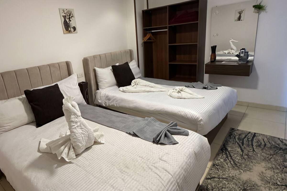 Two beds with white linens, black and white pillows, and folded towels.